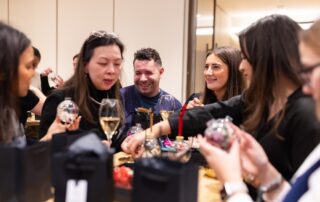 Colleagues gathered around a table with champagne, making dried flower baubles at a team Christmas party